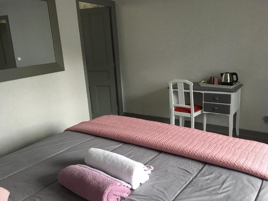 A bedroom with a bed, pillows, a chair, a desk, and a mirror.
