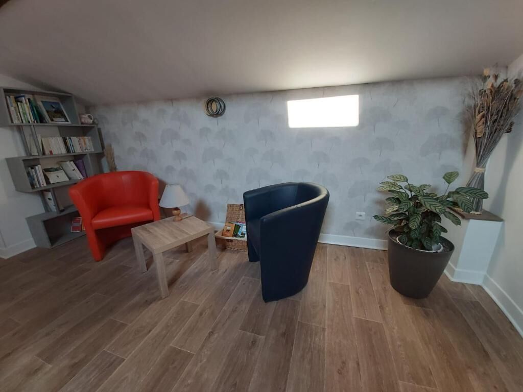 A room with a bookshelf, a red chair, a blue chair, a small table, and a potted plant.