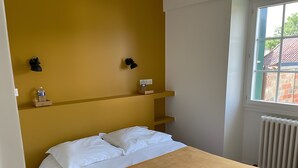 Un dormitorio con cama, ventana, radiador y dos lámparas fijadas a la pared.