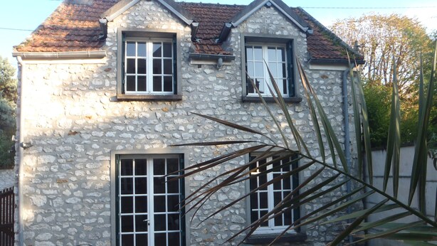 Una casa de piedra con estructura de dos pisos, una puerta principal y un pequeño patio con mesa y sillas.