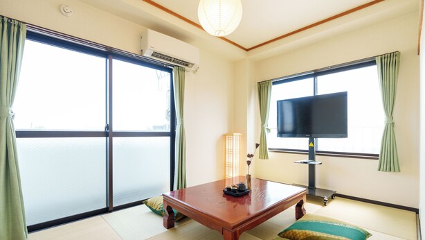 Una habitación con suelo de tatami, una mesa de madera, un televisor y puertas correderas.