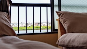 Habitación de hotel con una cama, una ventana que da a un río y edificios, y una barandilla de balcón.