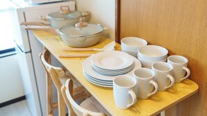 Una cocina con sillas de madera, una mesa con platos, tazones y tazas blancas apilados.