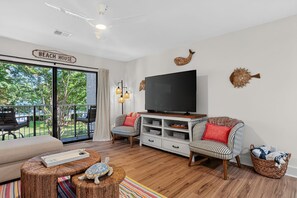 Ein Wohnzimmer mit Fernseher, gestreiften Sesseln, einem Holztisch und einem Schild mit der Aufschrift 'BEACH HOUSE'.