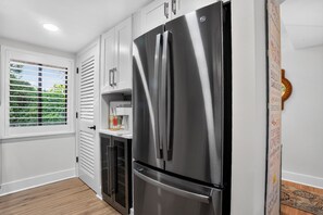 Eine Küche mit einem Edelstahl-Kühlschrank, weißen Schränken, einem Fenster mit Jalousien und einem kleinen Schrank mit einem Dekorationsgegenstand.