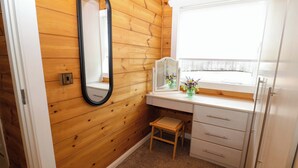 Een kleine kamer met houten lambrisering, een enkel bed, een nachtkastje met spiegel, een klein krukje en een raam.