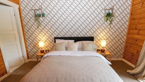 Een slaapkamer met een behang, een bed met hoofdeinde, twee nachtkastjes met lampen, en een deur.