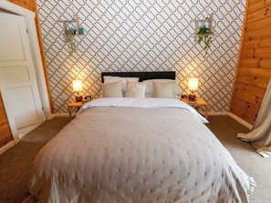 A bedroom with a patterned wall, a bed with a headboard, two bedside tables with lamps, and a door. - Bulrush Cabin (Carlisle)