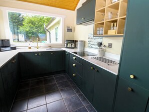 A kitchen with dark green cabinets, a white countertop, and a window overlooking a backyard. - Bulrush Cabin (Carlisle)