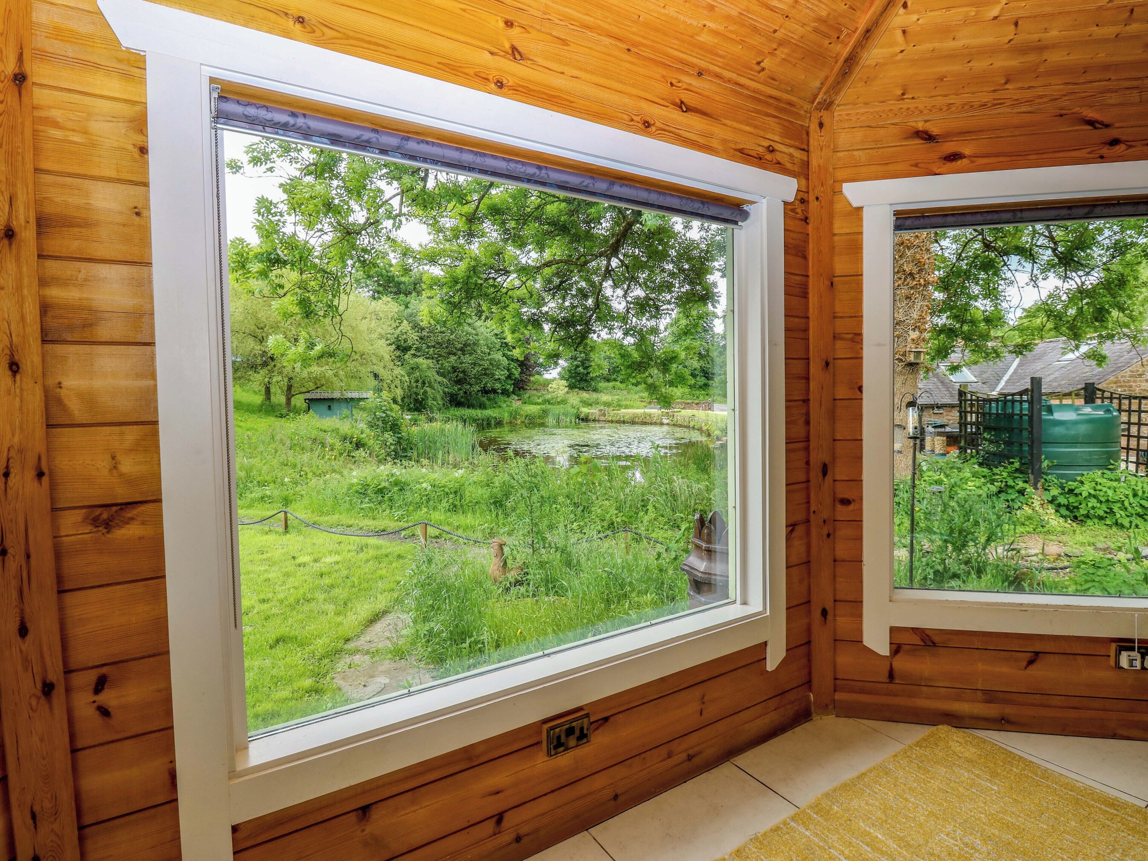 Una cabaña de madera con un ventanal grande que ofrece vistas a un estanque y vegetación.
