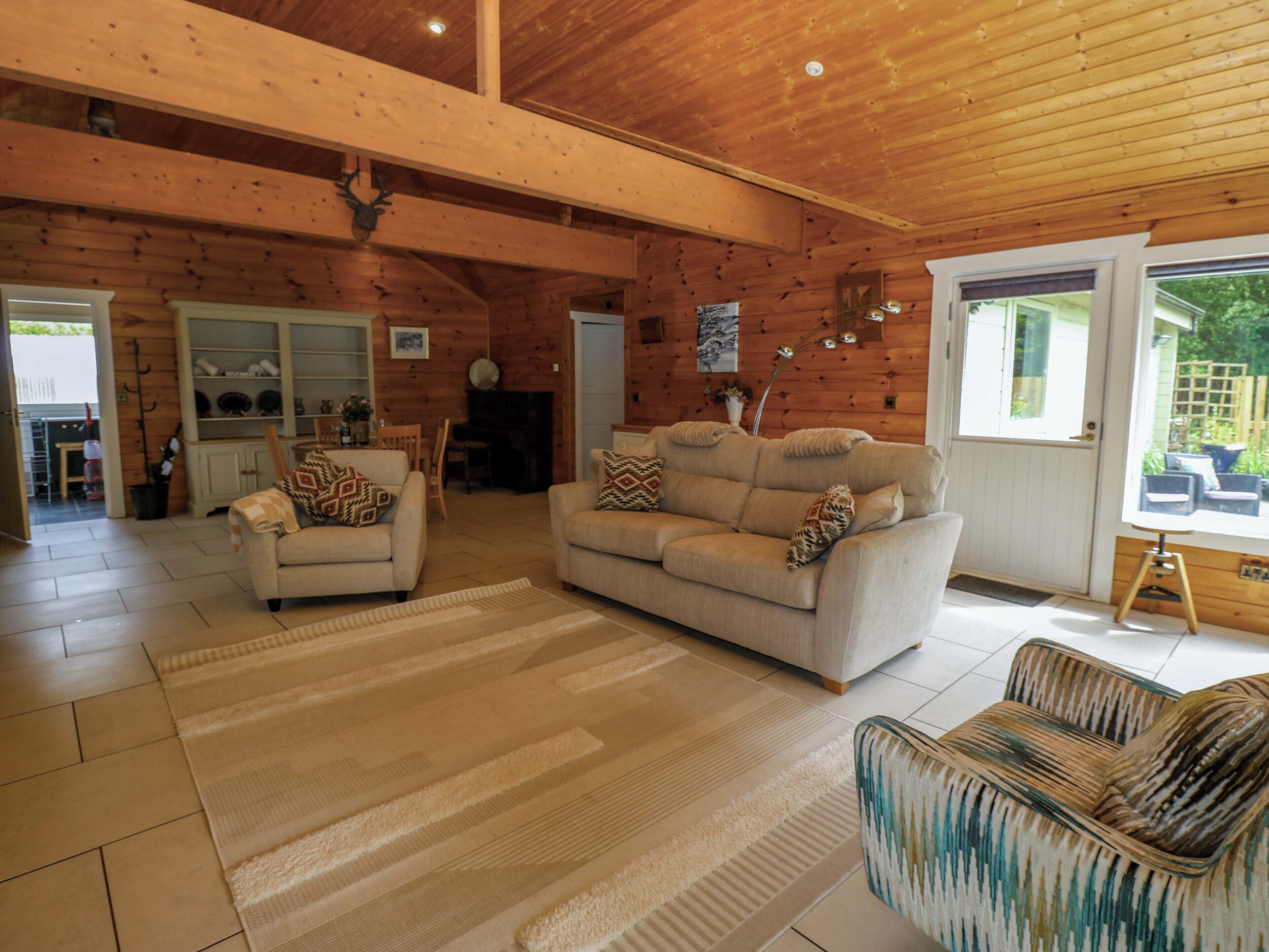 Amplia sala de estar con techo alto y paredes de madera, con dos sofás y un sillón estampado.