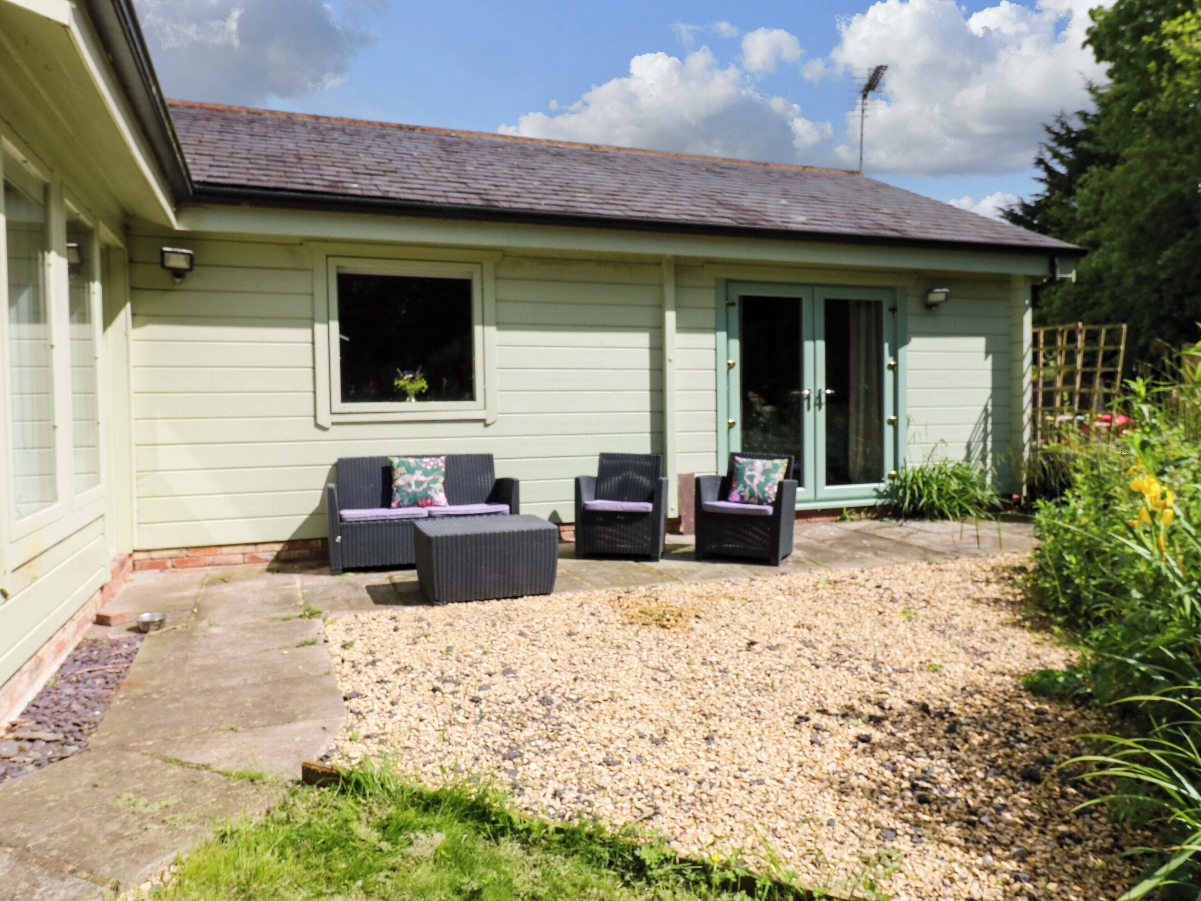 A building with a gravel patio, two wicker chairs with cushions, and a door with glass panels.