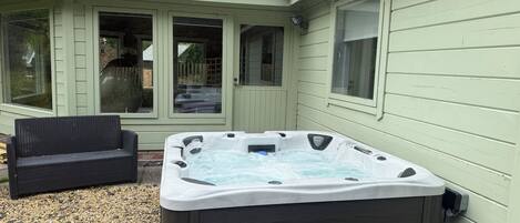 Un jacuzzi en un patio trasero con una silla de patio y un área de patio techada.