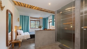Quarto de hotel moderno com cama, um banco de madeira, uma escrivaninha, área de chuveiro e um espelho grande.