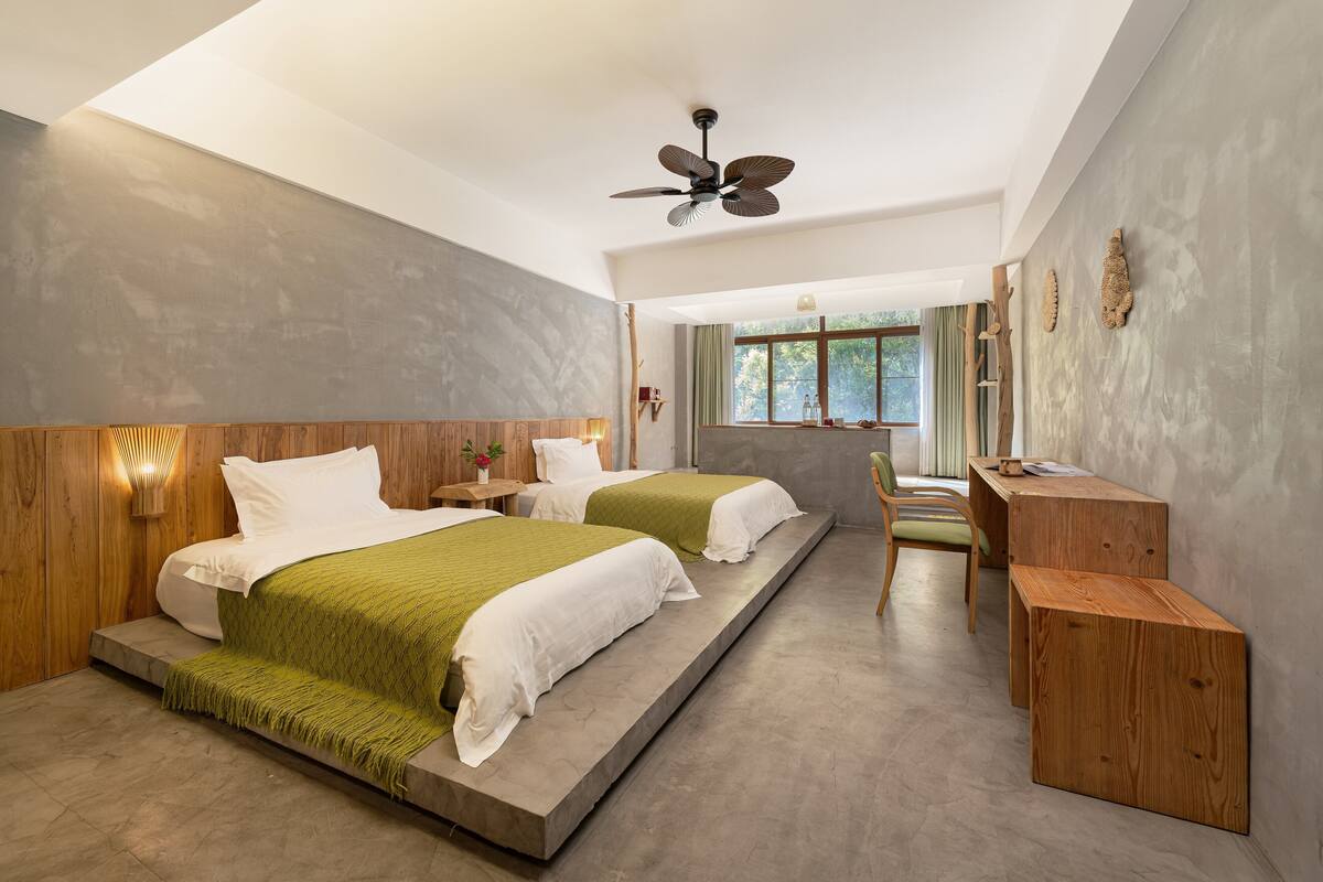A modern bedroom with two beds, a desk, and a ceiling fan.