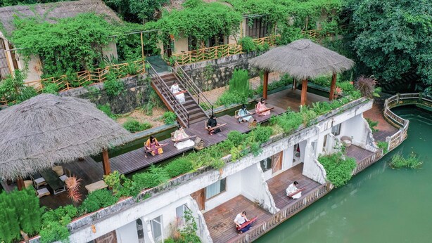 Uma casa flutuante com deck de madeira, estruturas de telhado de palha e um canal de água.