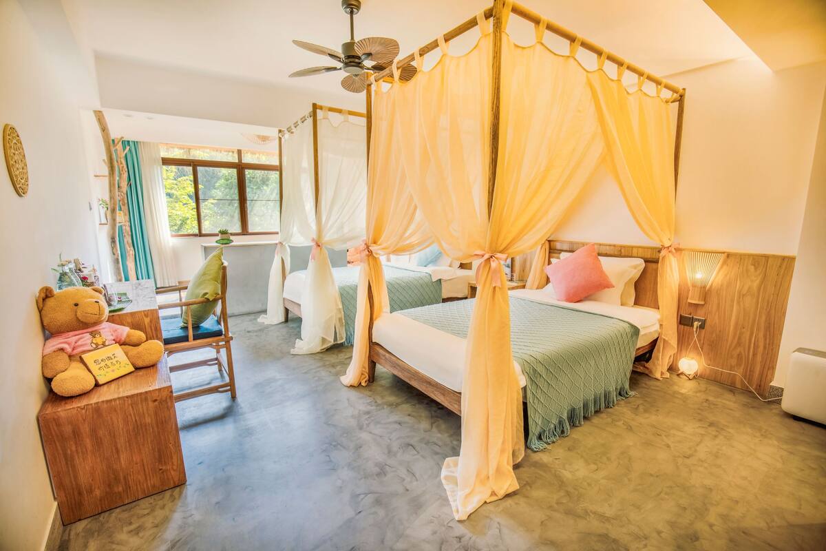 A room with a four-poster bed, a wooden bench with a teddy bear, and a ceiling fan.