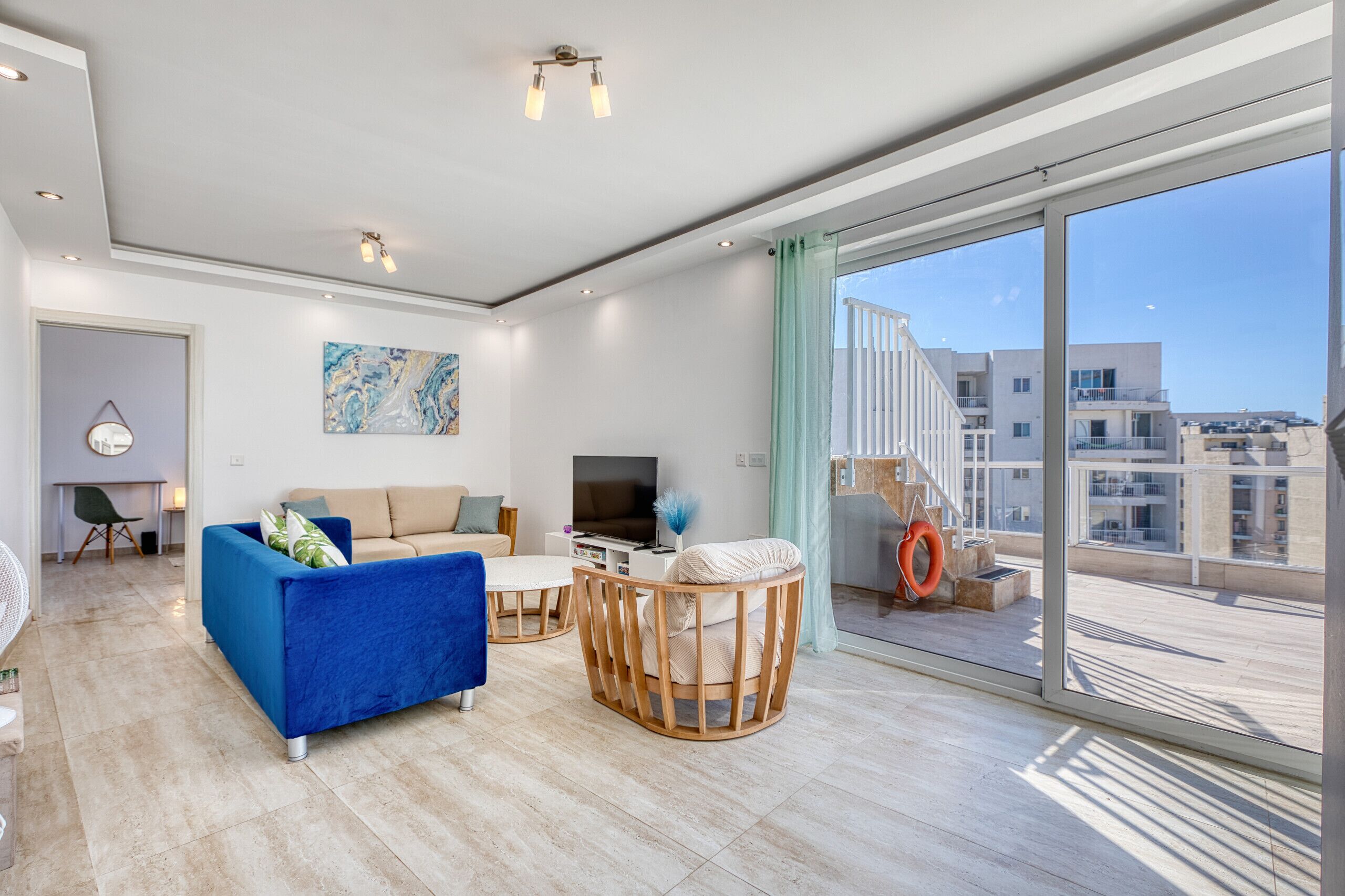 A modern living room with a sofa, a TV, and a large window with a view of buildings.