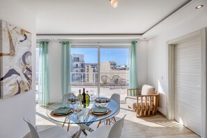 Ein moderner Essbereich mit einem Glastisch, Stühlen und Blick auf die Stadt durch große Fenster.