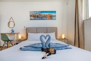 Ein Hotelzimmer mit Bett, einem Stadtbildgemälde, einem Spiegel, einem Sessel und einem Nachttisch mit Lampe.