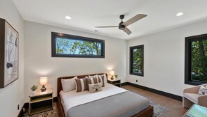 A modern bedroom with a large bed, two bedside tables with lamps, a ceiling fan, and large windows. - Willow Landing (Troutman)