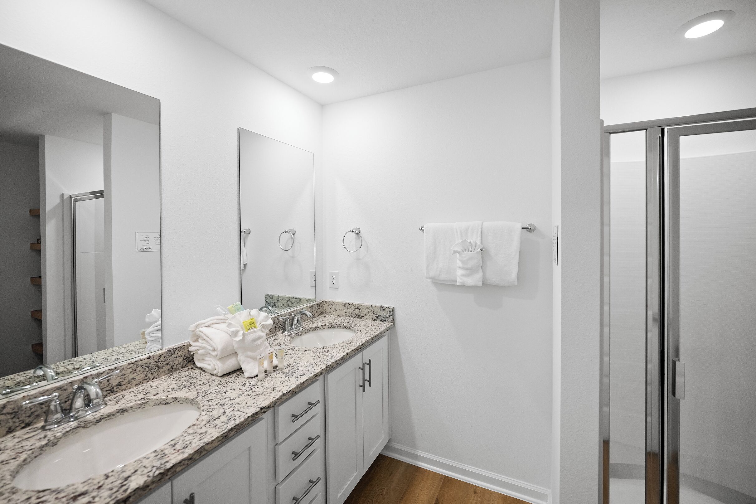 A modern bathroom with two sinks, a large mirror, and a glass shower enclosure.