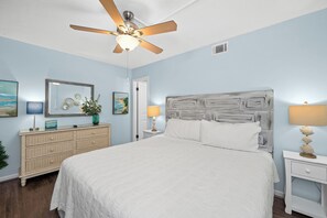 Ein Schlafzimmer mit Bett, Schminktisch, Nachttisch, Deckenventilator und Wandbildern.