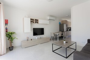 Un saló modern amb televisió de pantalla plana, zona de menjador amb taula i cadires, i cuina al fons.