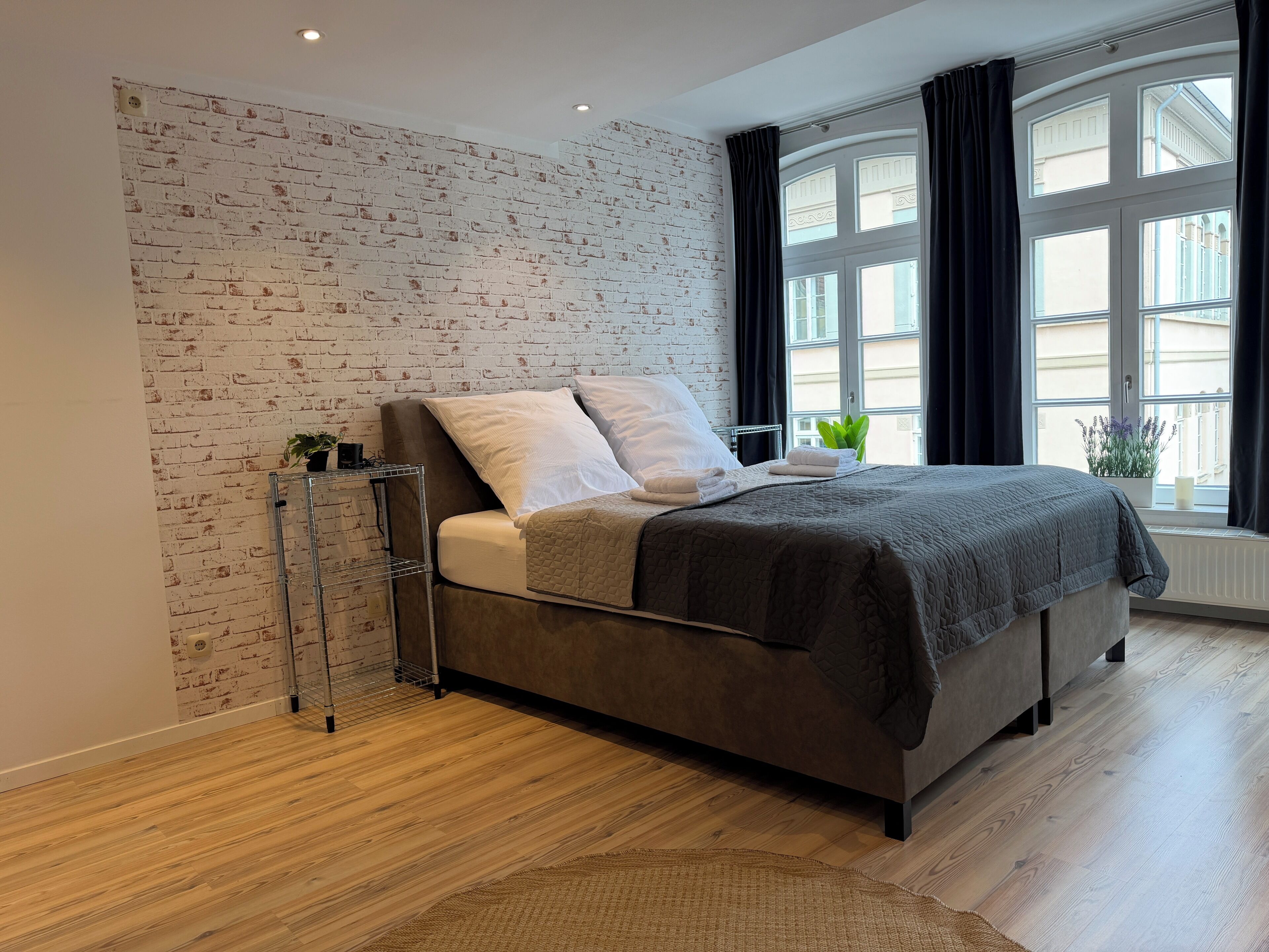 Ein modernes Schlafzimmer mit einer Ziegelwand, einem Bett mit dunklem Kopfteil und einem Fenster mit Vorhängen.