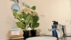 Un bagno con lavandino bianco, uno specchio, una pianta in vaso e un dispenser per sapone.