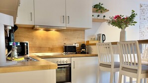 Una cucina moderna con mobili bianchi, un piano di lavoro in legno, un forno Bosch, un tostapane e una macchina per il caffè. Ci sono due sedie bianche e un vaso con fiori sul bancone.
