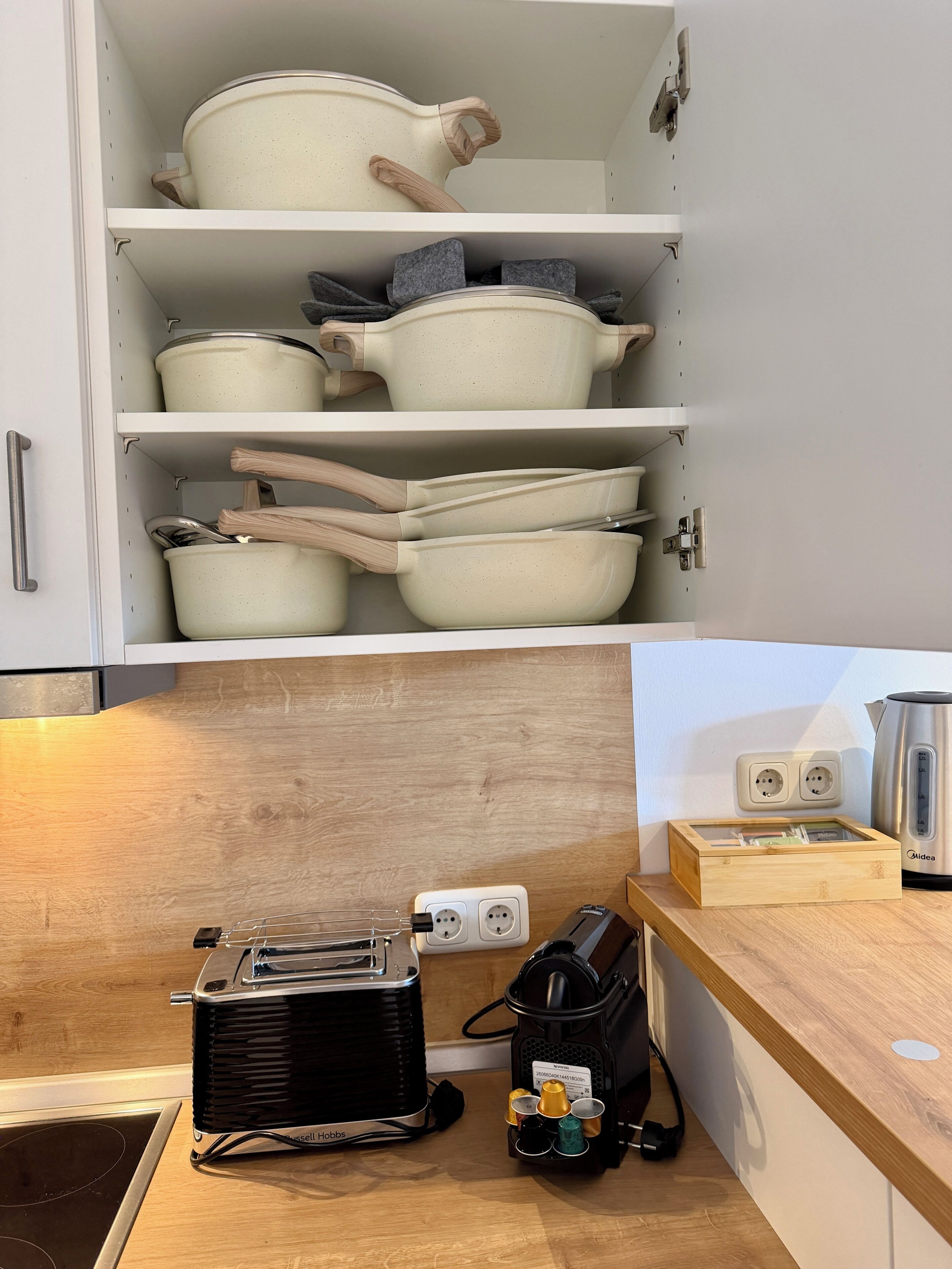 Et køkken med hvide skabe, en træbordplade, en elkedel, en kaffemaskine og en transportabel gasblus.