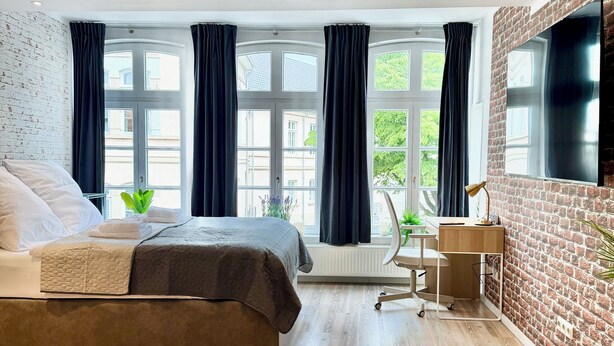 Una camera da letto moderna con un letto, una scrivania e un'ampia finestra con tende.