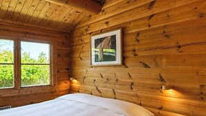 Une chambre dans une cabane en bois, avec un lit, un tableau encadré au mur et une petite table.
