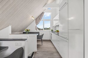 A modern kitchen with a sloped ceiling, white cabinetry, and a view of the outdoors. - "Seeschwalbe" Marina Wendtorf holiday home by the beach with sea view (Wendtorf)