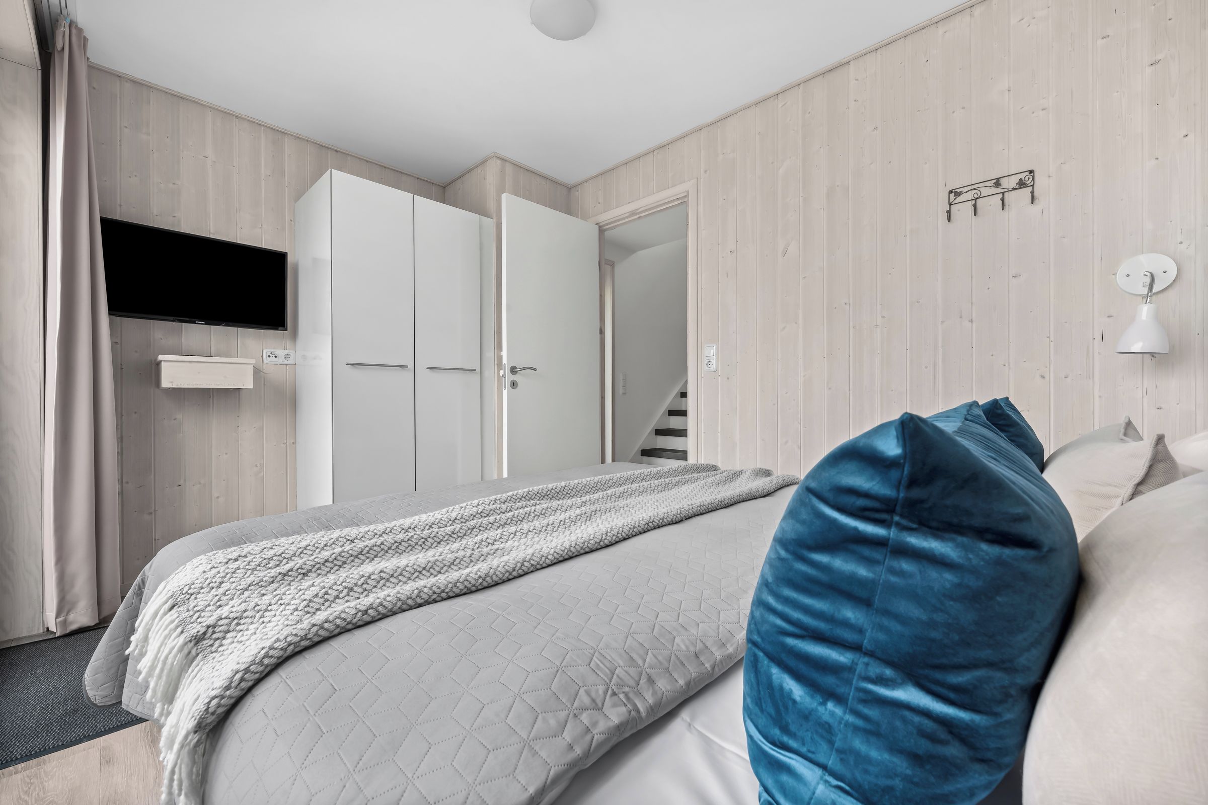 A bedroom with a bed, a TV mounted on the wall, a door, and a light fixture.