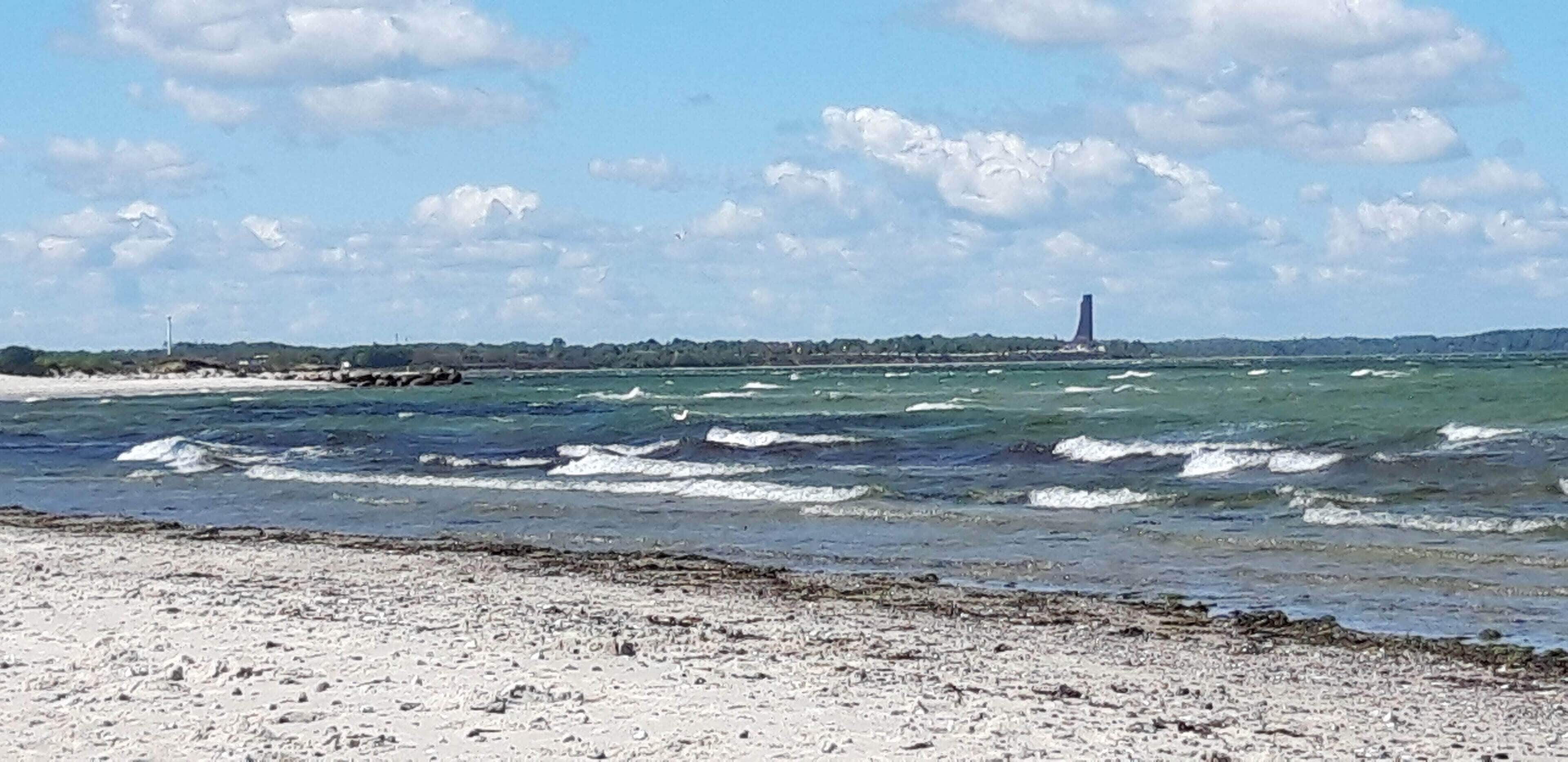 A beach with waves, a distant tower, and a clear sky.