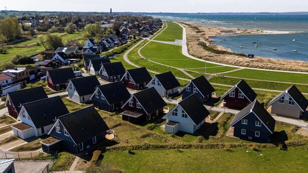 Ein Küstenwohngebiet mit Häusern, die entlang einer gewundenen Straße in Reih und Glied angeordnet sind, führt zu einem Strand mit Booten.