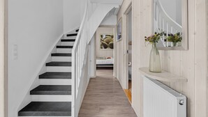 Uma escadaria leva a um quarto com uma cama, um radiador e um vaso de flores sobre uma prateleira.