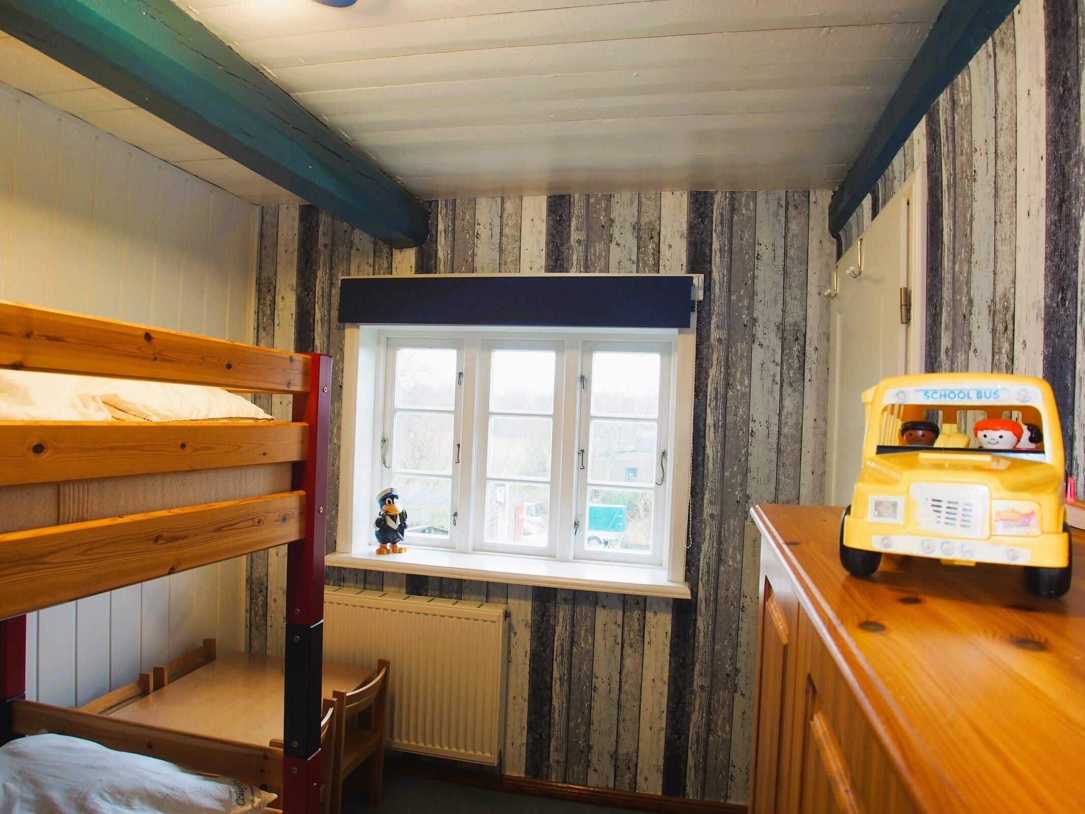 Um quarto com beliches, uma janela com vista, um radiador e um ônibus escolar de brinquedo.