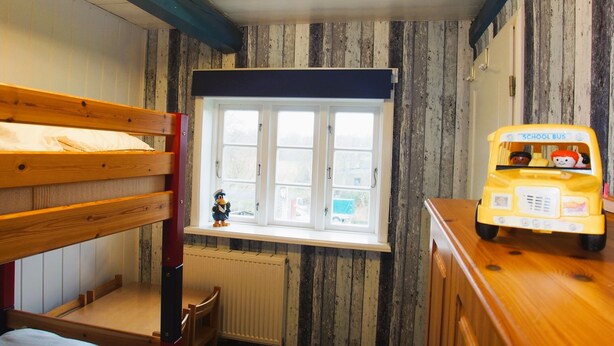Ein Zimmer mit Etagenbetten, einem Fenster mit Blick, einem Heizkörper und einem Spielzeug-Schulbus.