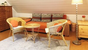 Ein gemütliches Schlafzimmer im Loft-Stil mit einer Couch, zwei Korbstühlen, einem kleinen runden Tisch und einer Stehlampe.