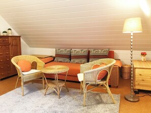 A cozy loft bedroom with a sofa, two wicker chairs, a small round table, and a floor lamp. - Ferienhaus auf der kleinen Gaarde  – sauna, washing machine, garden, fireplace (Ockholm)