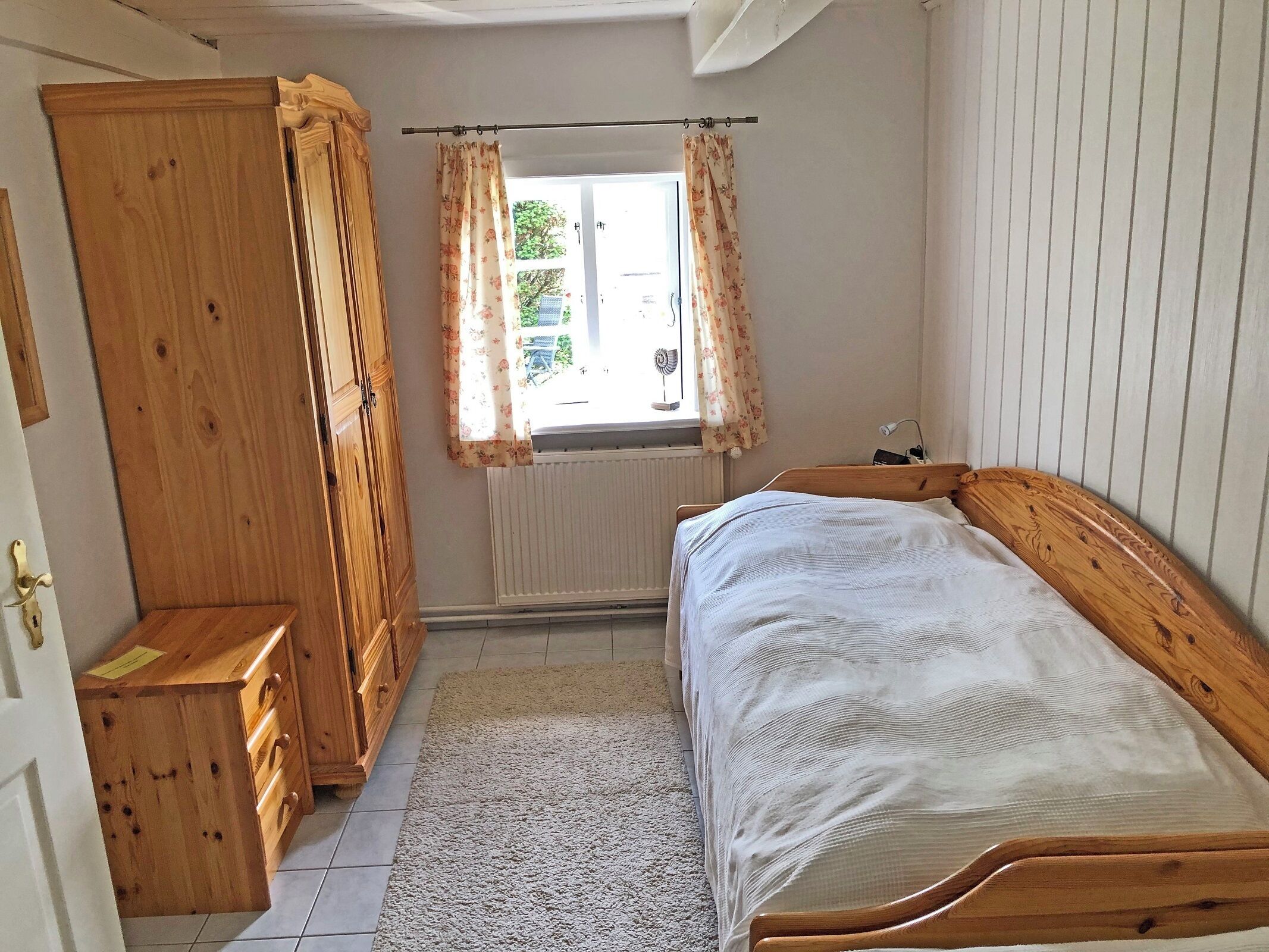 Una camera da letto con un letto di legno, un armadio, un termosifone e una finestra con tende.
