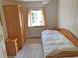 A bedroom with a wooden bed, a wardrobe, a radiator, and a window with curtains.