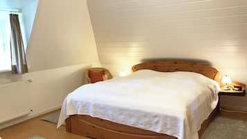 Ein Schlafzimmer mit einem hölzernen Bett, einem Nachttisch mit Lampe, einem Fenster mit Vorhängen und einer Heizung.