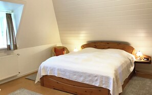 Ein Schlafzimmer mit einem hölzernen Bett, einem Nachttisch mit Lampe, einem Fenster mit Vorhängen und einer Heizung.