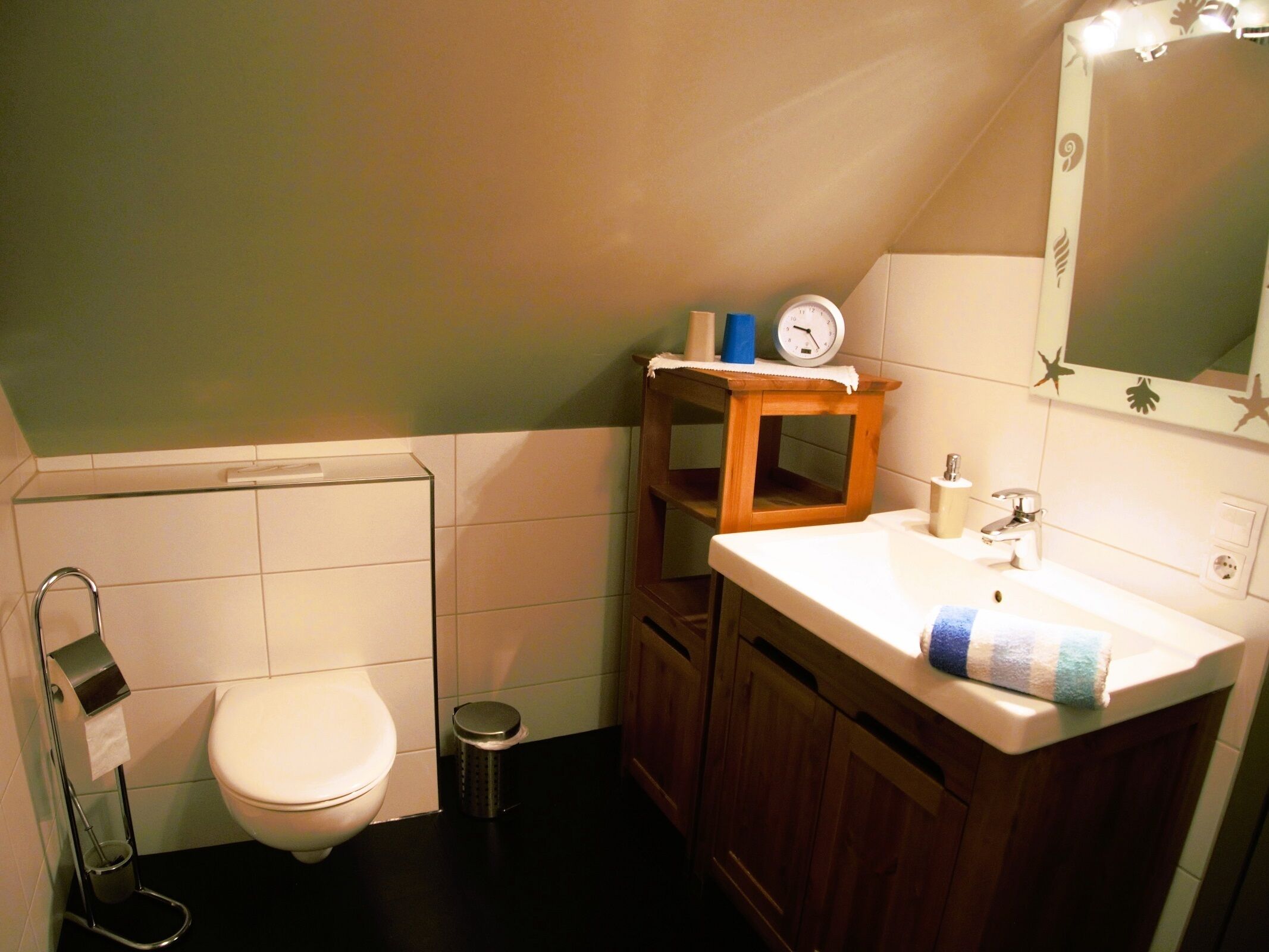 Een kleine badkamer met toilet, wastafel, spiegel en een klok aan de muur.