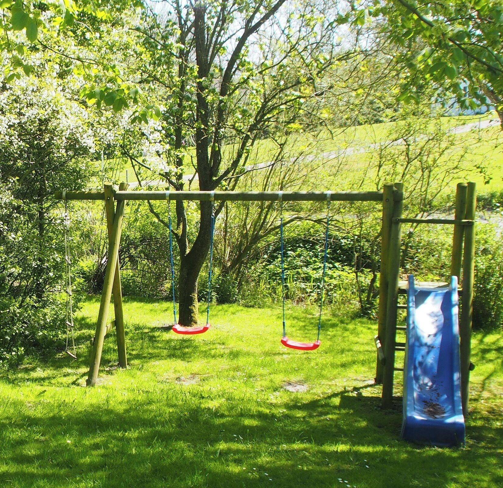 Ein Spielplatz mit Schaukeln und einer Rutsche, umgeben von grünem Gras und Bäumen.