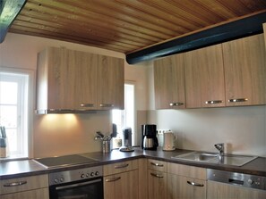 A kitchen with wooden cabinets, stainless steel appliances, and a window providing natural light. - Ferienhaus auf der kleinen Gaarde  – sauna, washing machine, garden, fireplace (Ockholm)